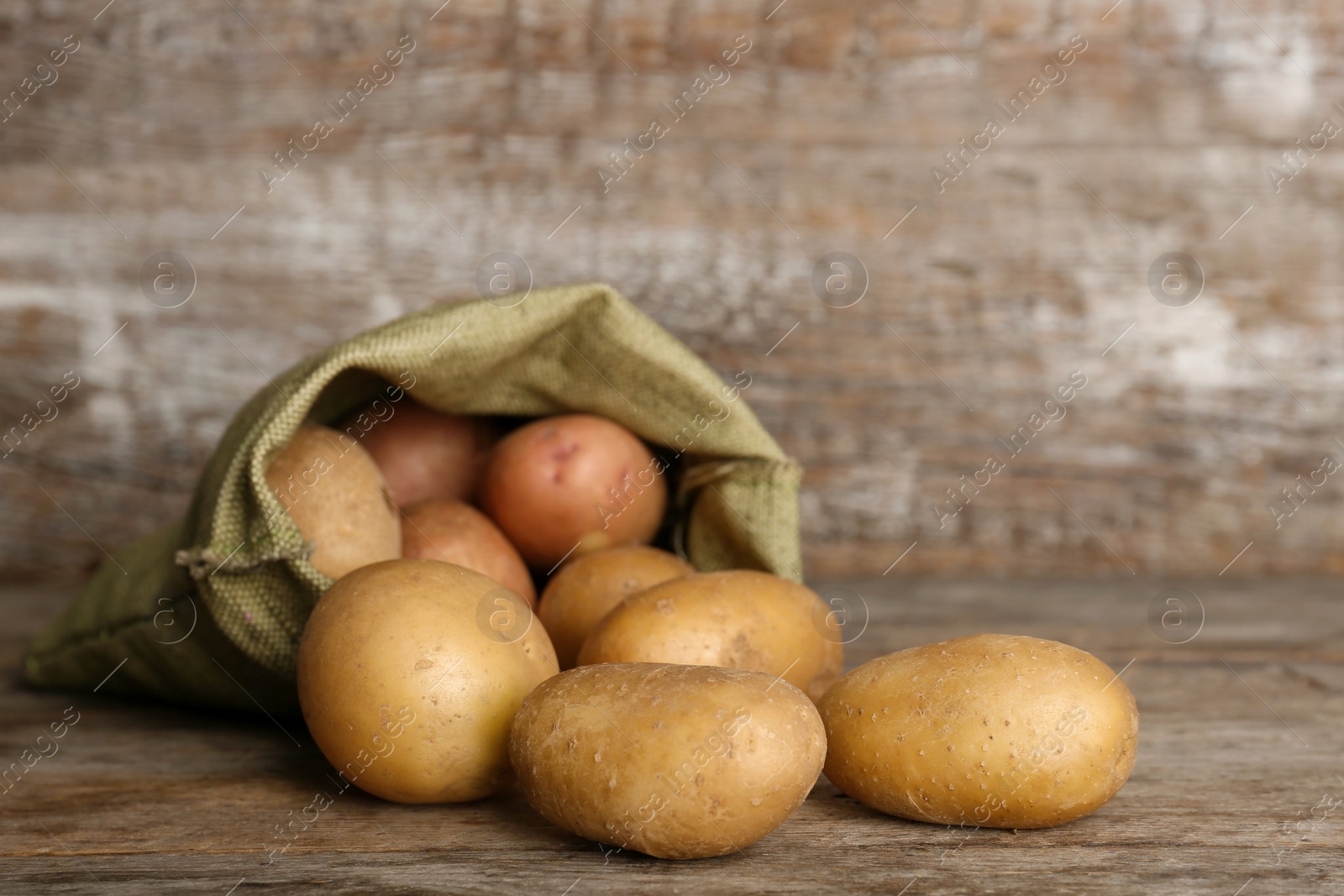 Photo of Sack with fresh ripe organic potatoes on wooden table