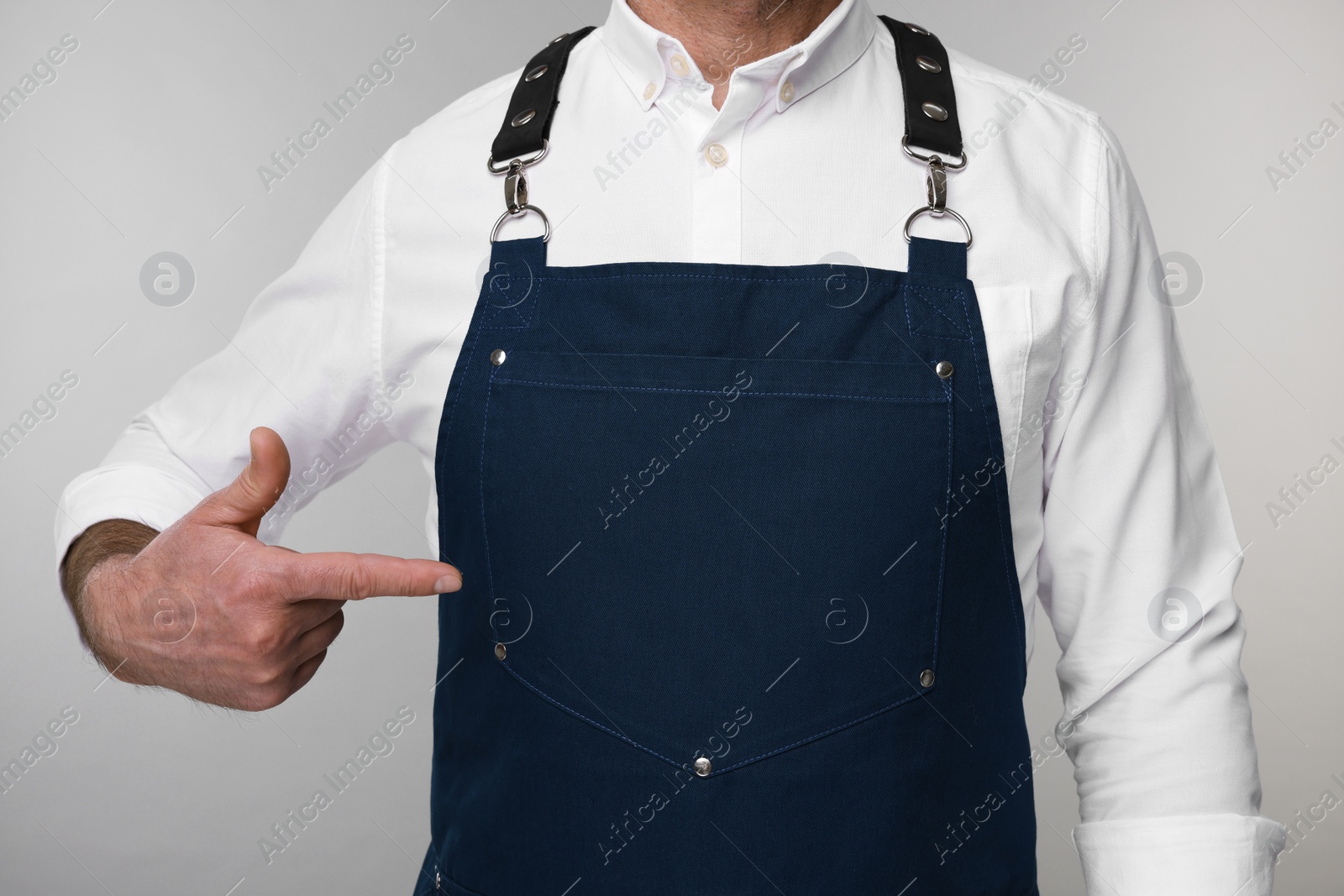Photo of Man pointing at kitchen apron on grey background, closeup. Mockup for design