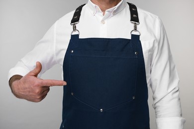 Man pointing at kitchen apron on grey background, closeup. Mockup for design