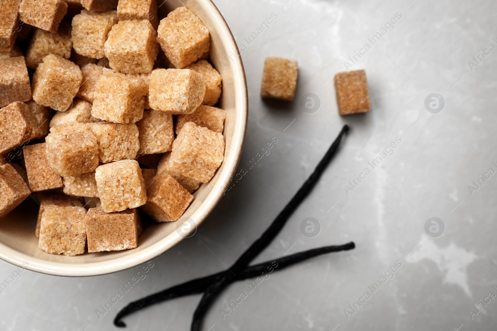 Photo of Bowl of aromatic vanilla lump sugar and sticks on grey background