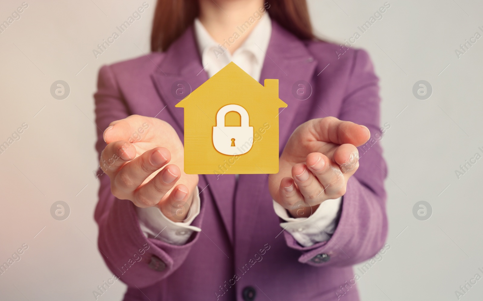 Image of Home security concept. Woman holding house on light background, closeup