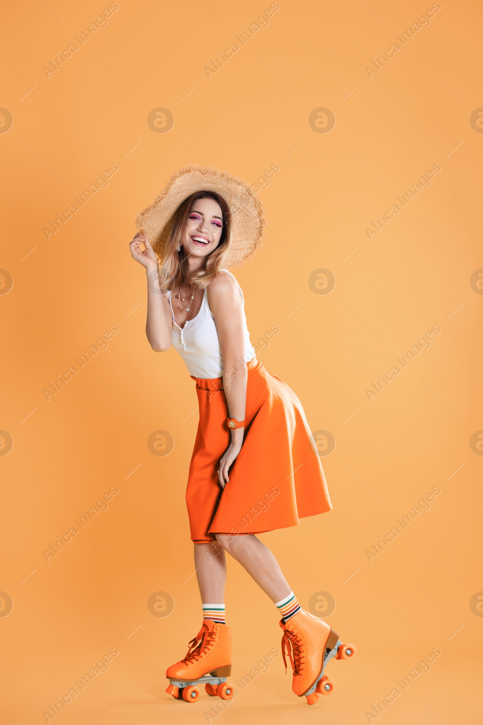 Image of Young woman with retro roller skates on orange background