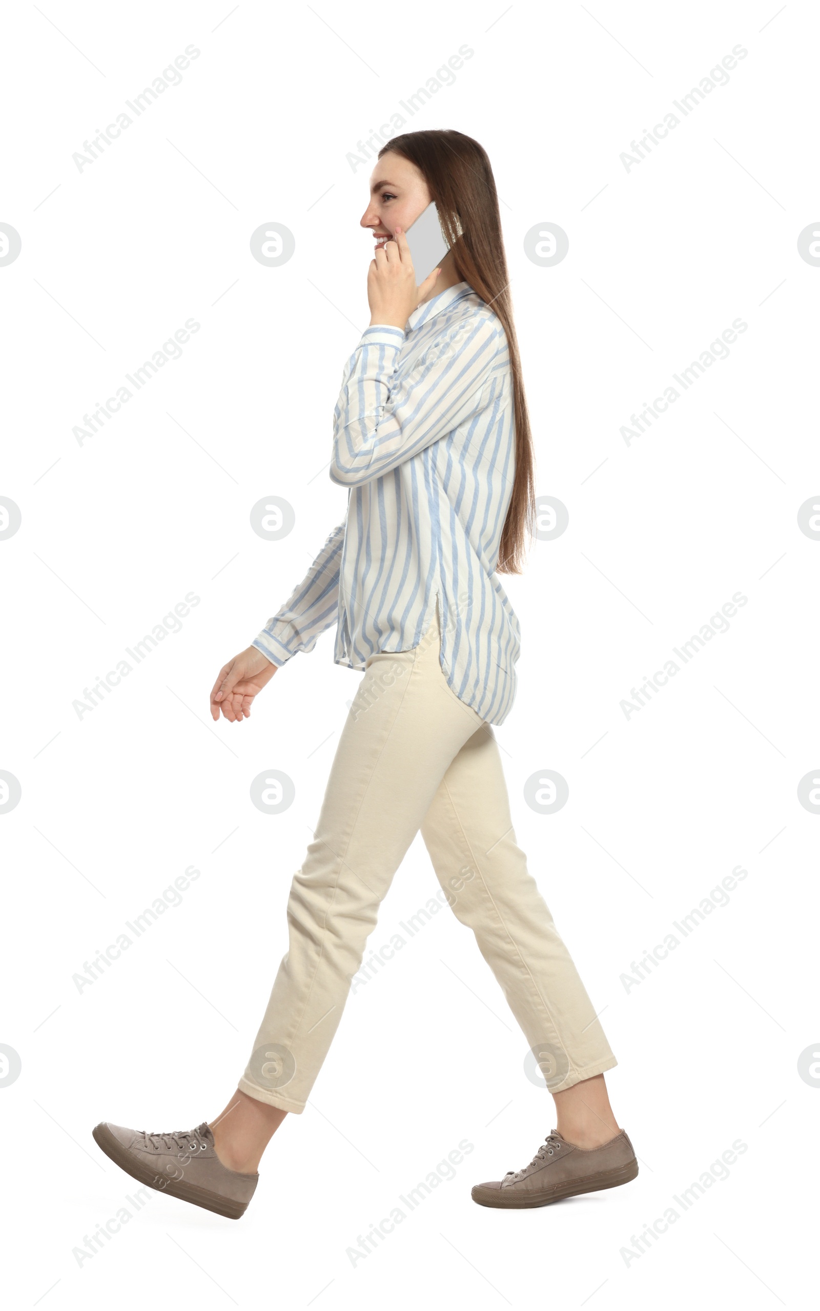 Photo of Young woman in casual outfit talking on smartphone while walking against white background