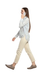 Young woman in casual outfit talking on smartphone while walking against white background