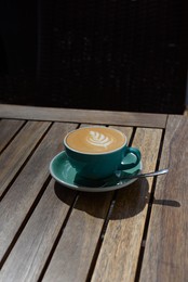 Photo of Cup of aromatic hot coffee and spoon on wooden table in outdoor cafe