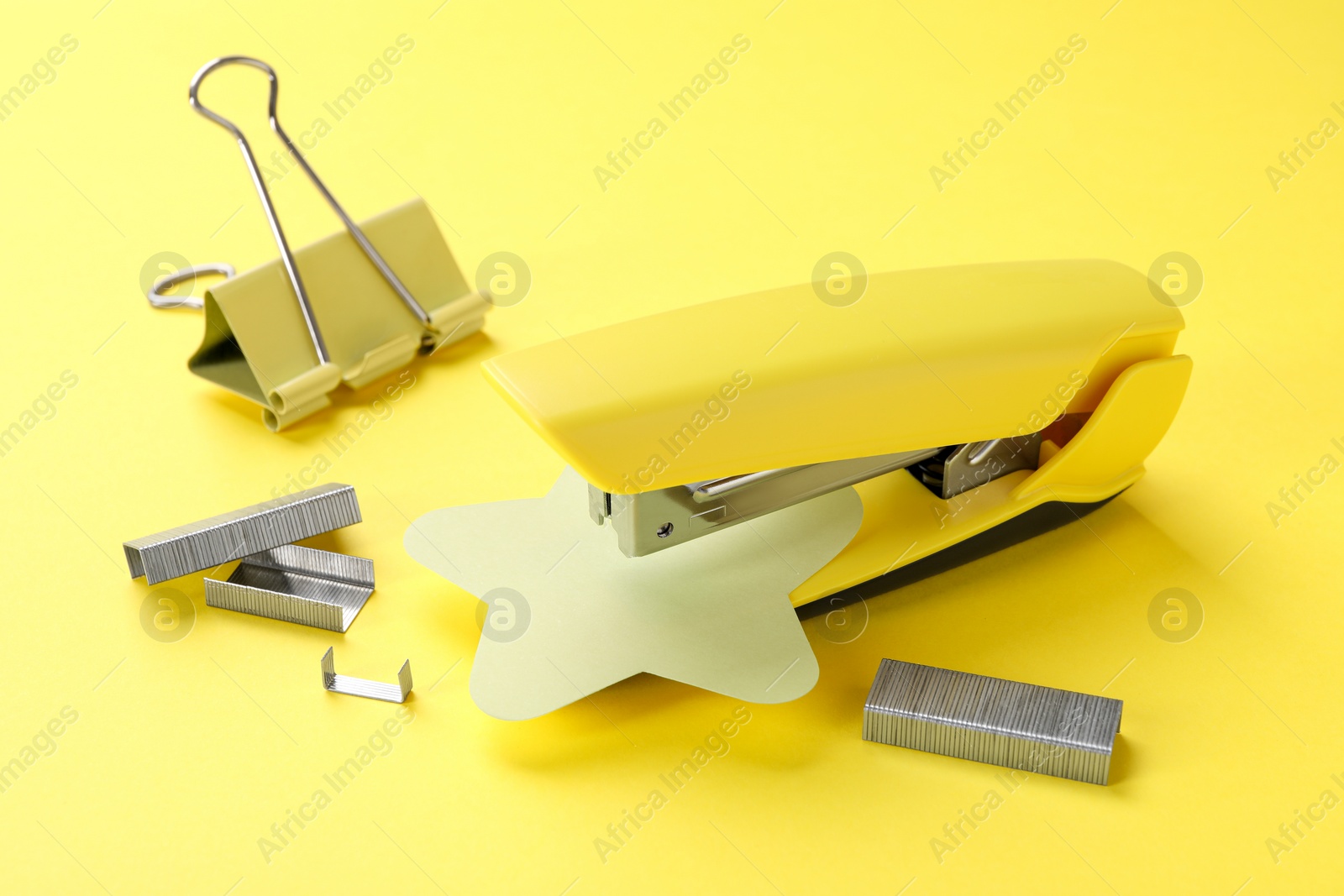 Photo of Stapler with staples and binder clip on yellow background, closeup