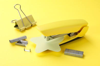 Stapler with staples and binder clip on yellow background, closeup