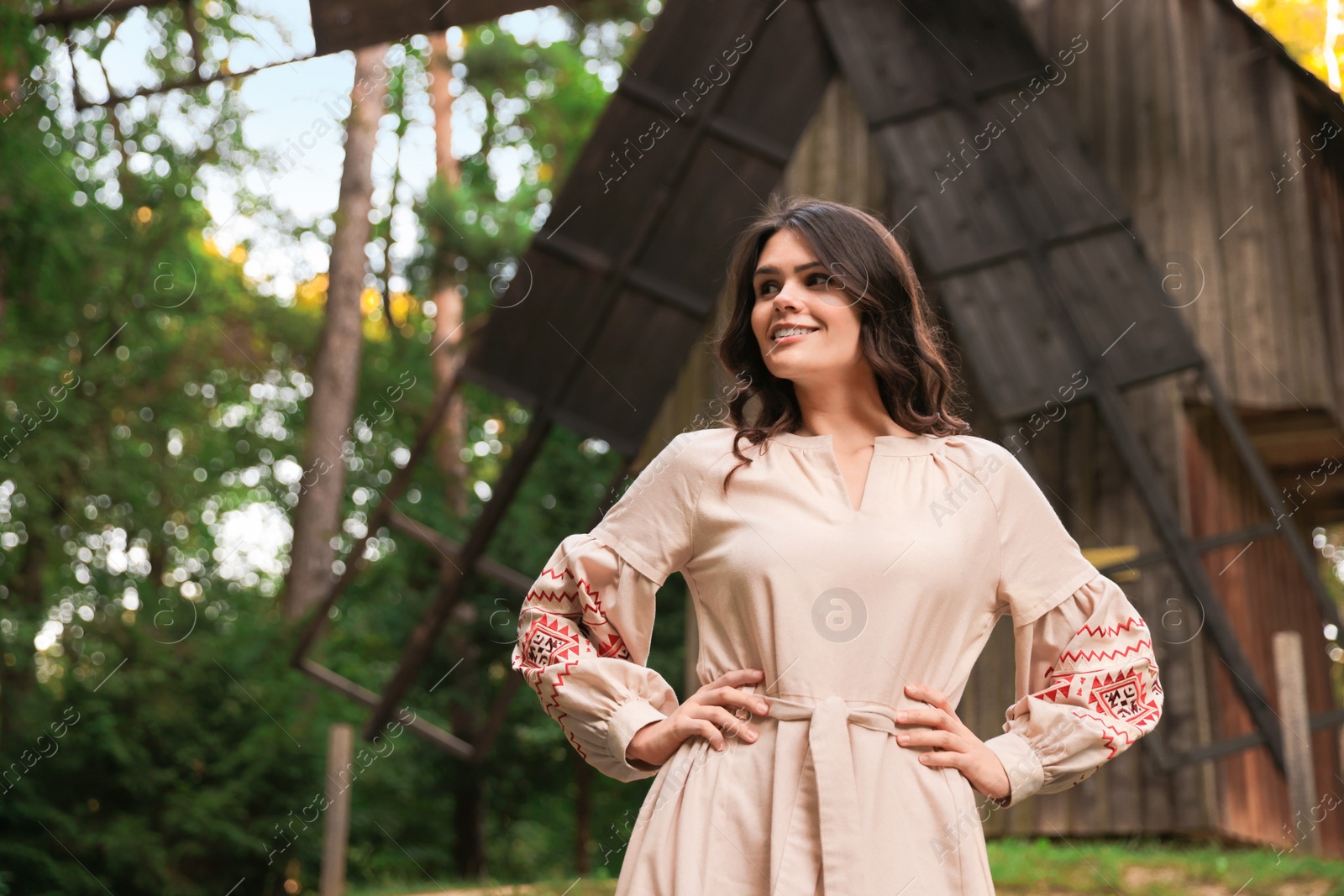 Photo of Beautiful woman wearing embroidered dress near old wooden mill in countryside. Ukrainian national clothes