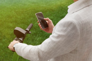 Photo of Businessman with modern kick scooter using smartphone outdoors, closeup
