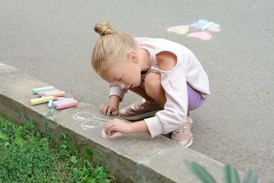 Photo of Little child drawing balloons with chalk on asphalt