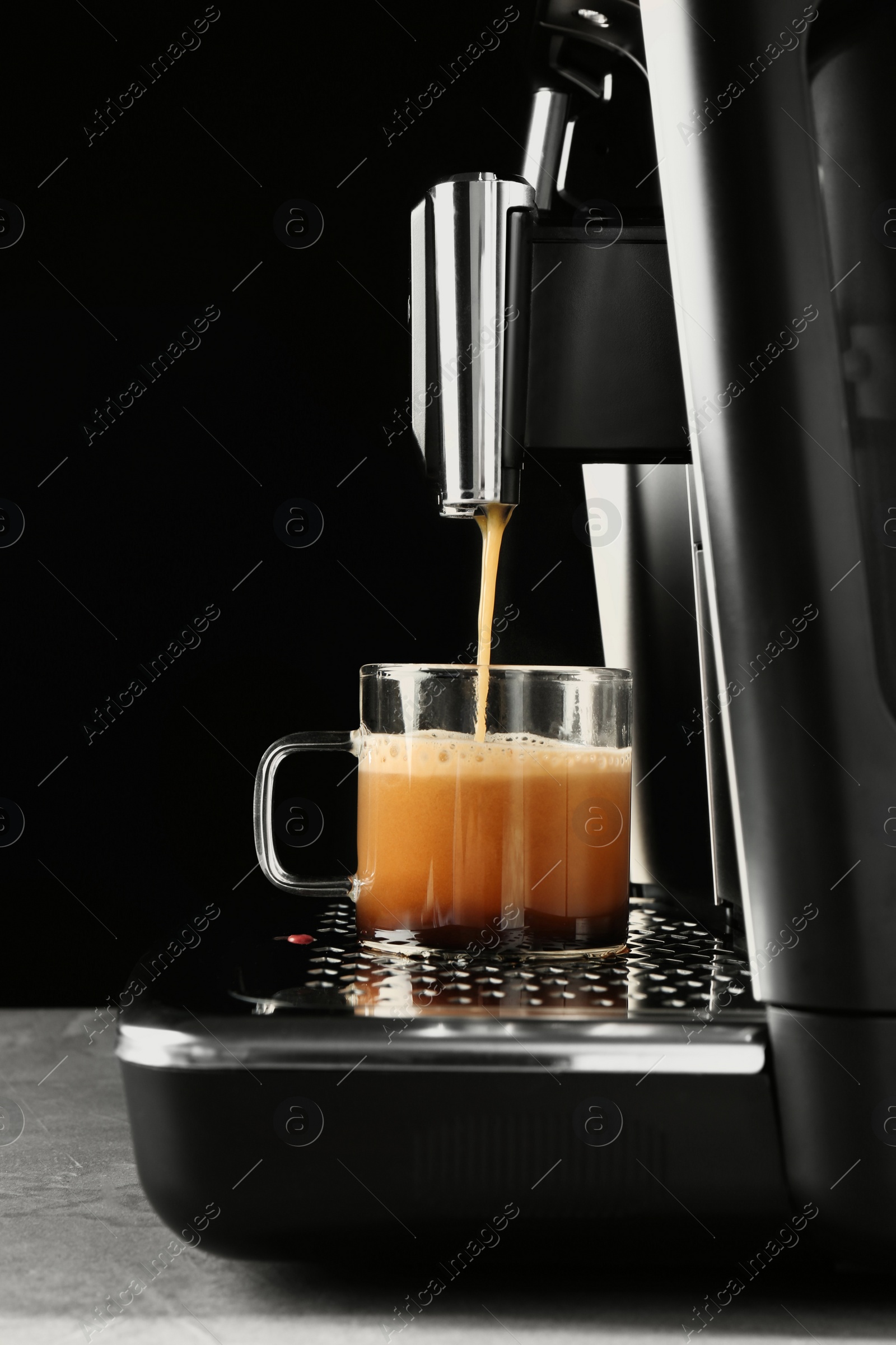 Photo of Modern espresso machine pouring coffee into glass cup on grey table against black background