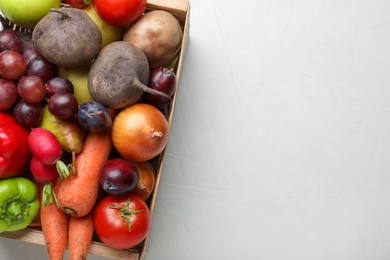 Photo of Wooden crate full of harvested vegetables and fruits on light table, top view. Space for text