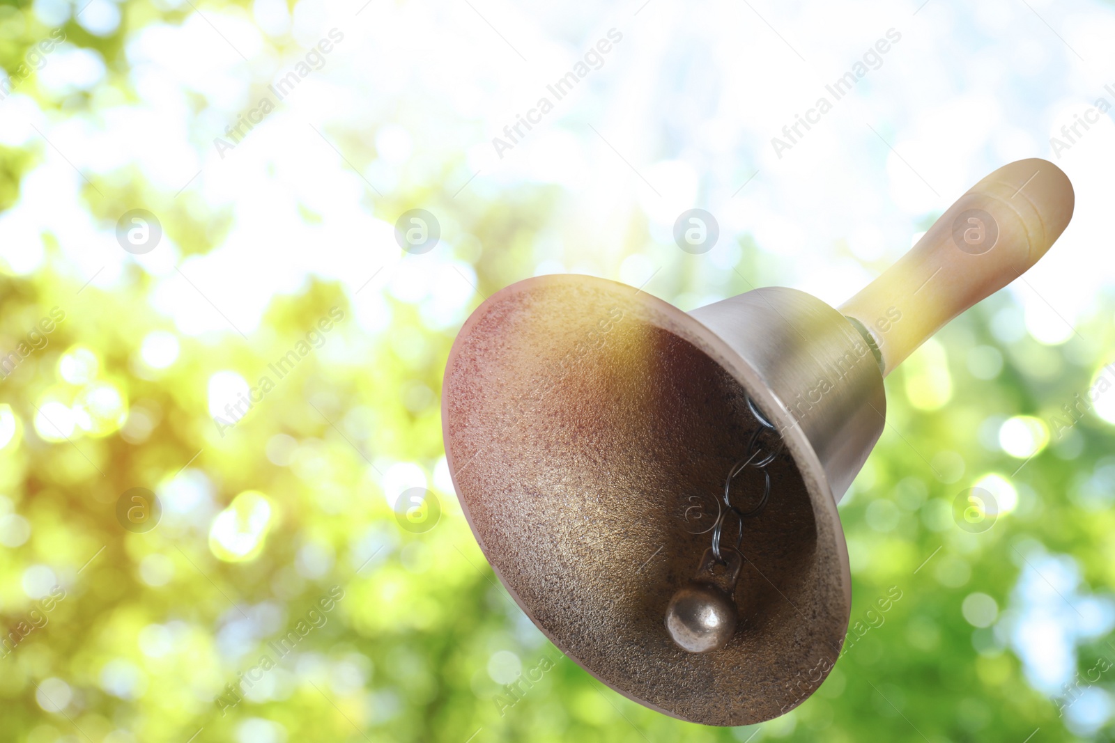 Image of Shiny school bell with wooden handle outdoors, space for text. Bokeh effect