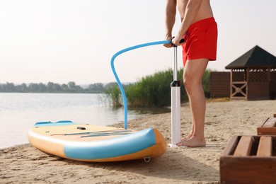 Man pumping up SUP board on river shore, closeup