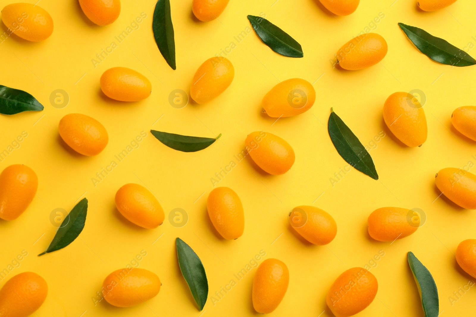 Photo of Fresh ripe kumquats with green leaves on yellow background, flat lay