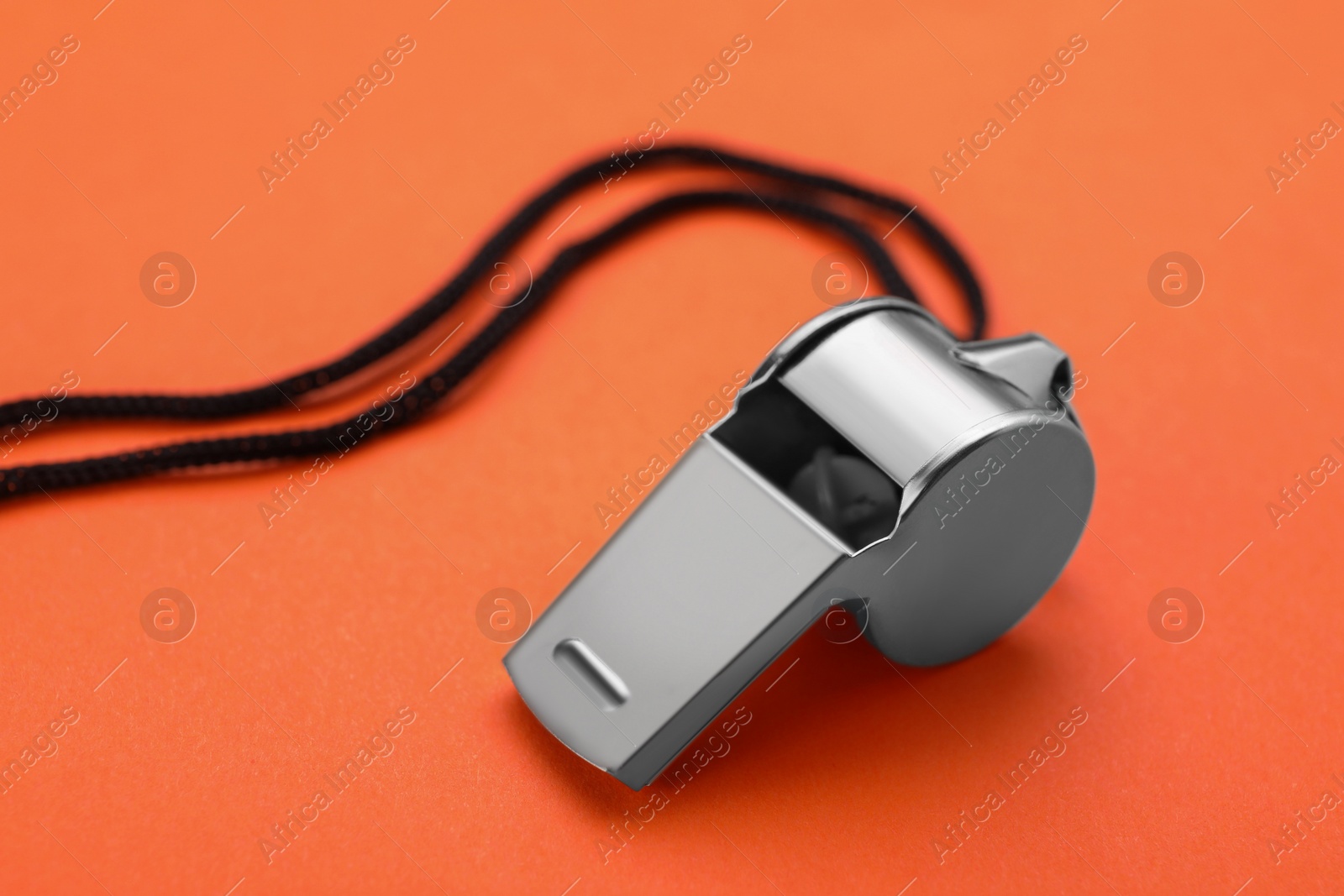 Photo of One metal whistle with black cord on orange background, closeup