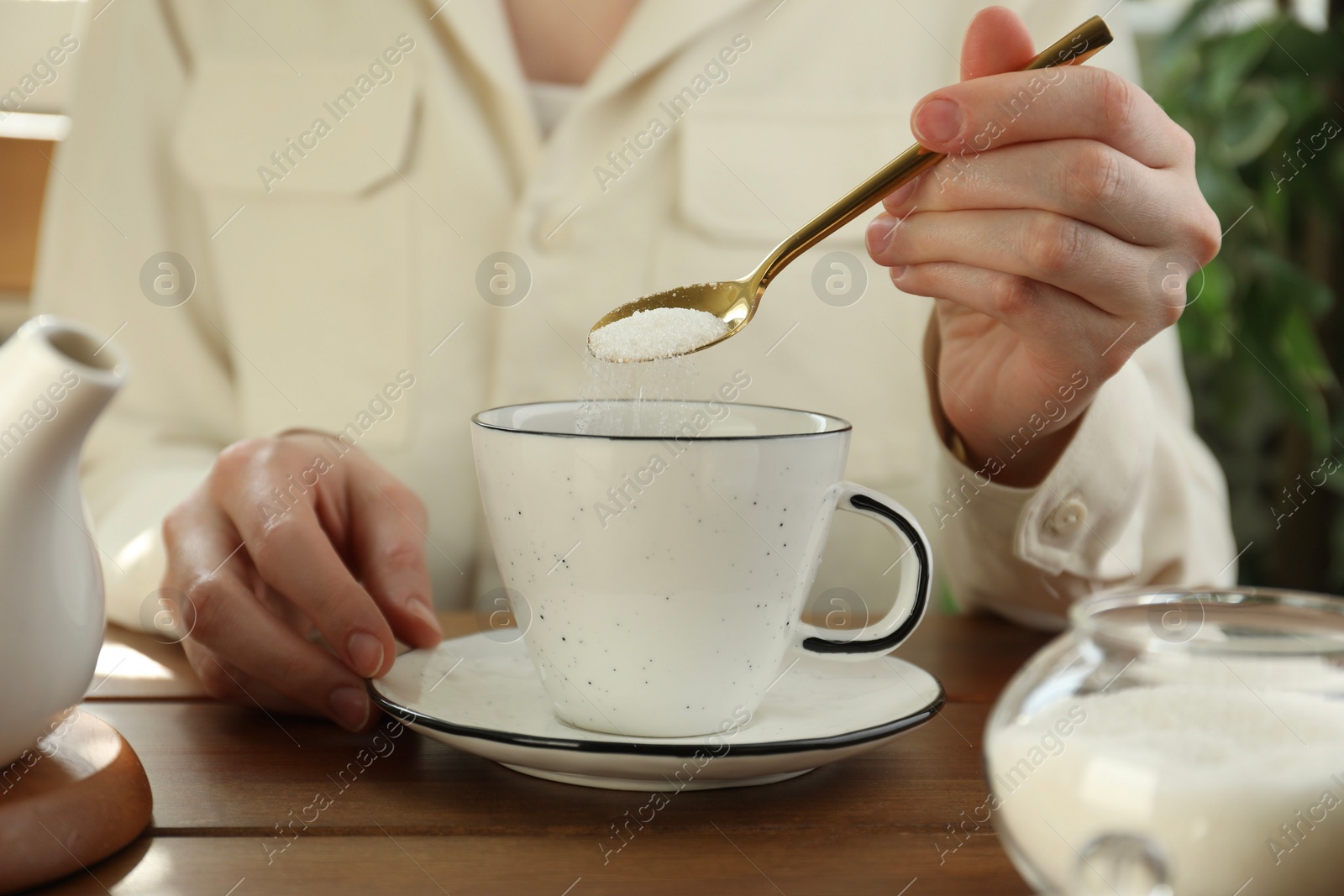 Photo of Woman adding sugar into aromatic tea at wooden table indoors, closeup