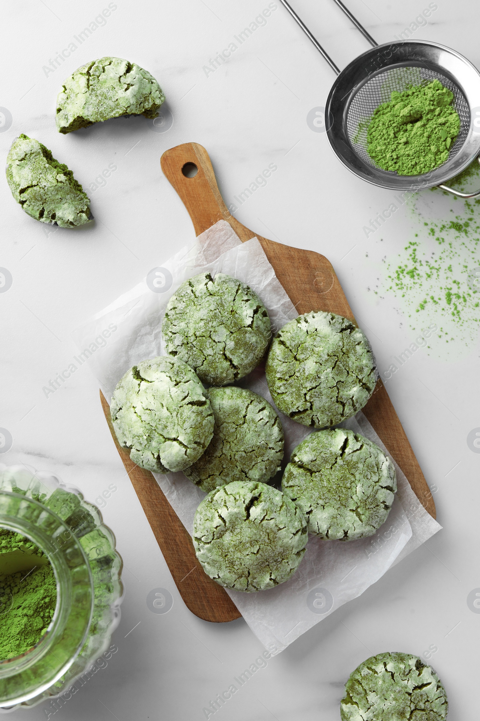 Photo of Board with tasty matcha cookies and powder on white marble table, flat lay
