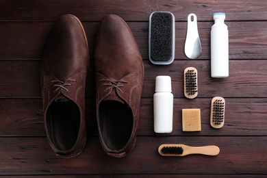 Stylish footwear with shoe care accessories on brown wooden table, flat lay