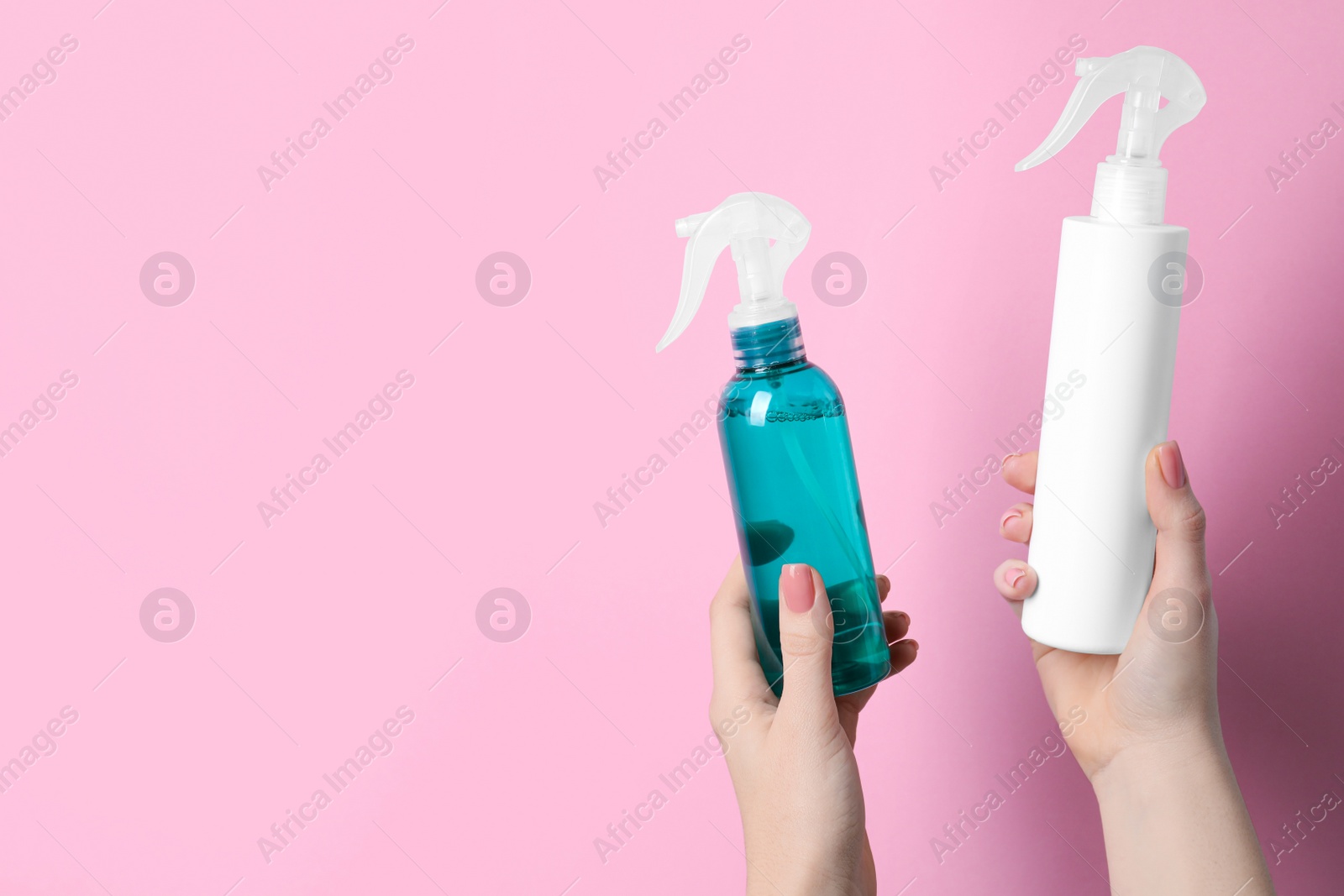Photo of Woman holding spray bottles with thermal protection on light pink background, closeup. Space for text