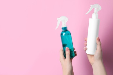 Woman holding spray bottles with thermal protection on light pink background, closeup. Space for text