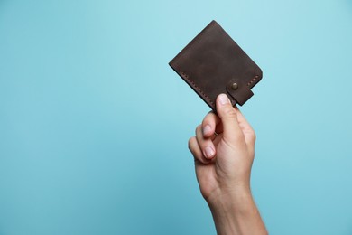 Photo of Man holding leather wallet on light blue background, closeup. Space for text
