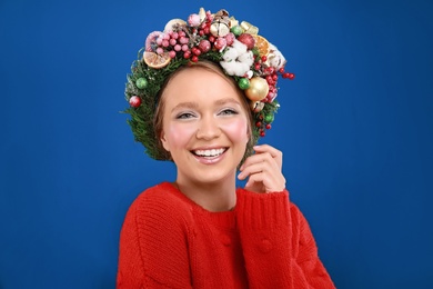 Photo of Beautiful young woman wearing Christmas wreath on blue background