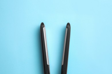 Photo of Modern flat hair iron on light blue background, top view