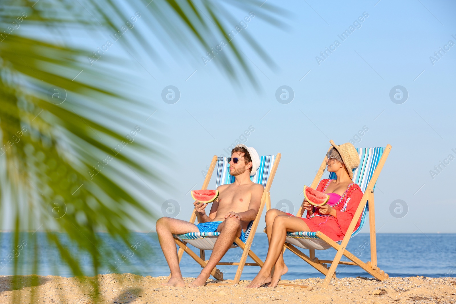 Photo of Young couple with watermelon slices in beach chairs at seacoast