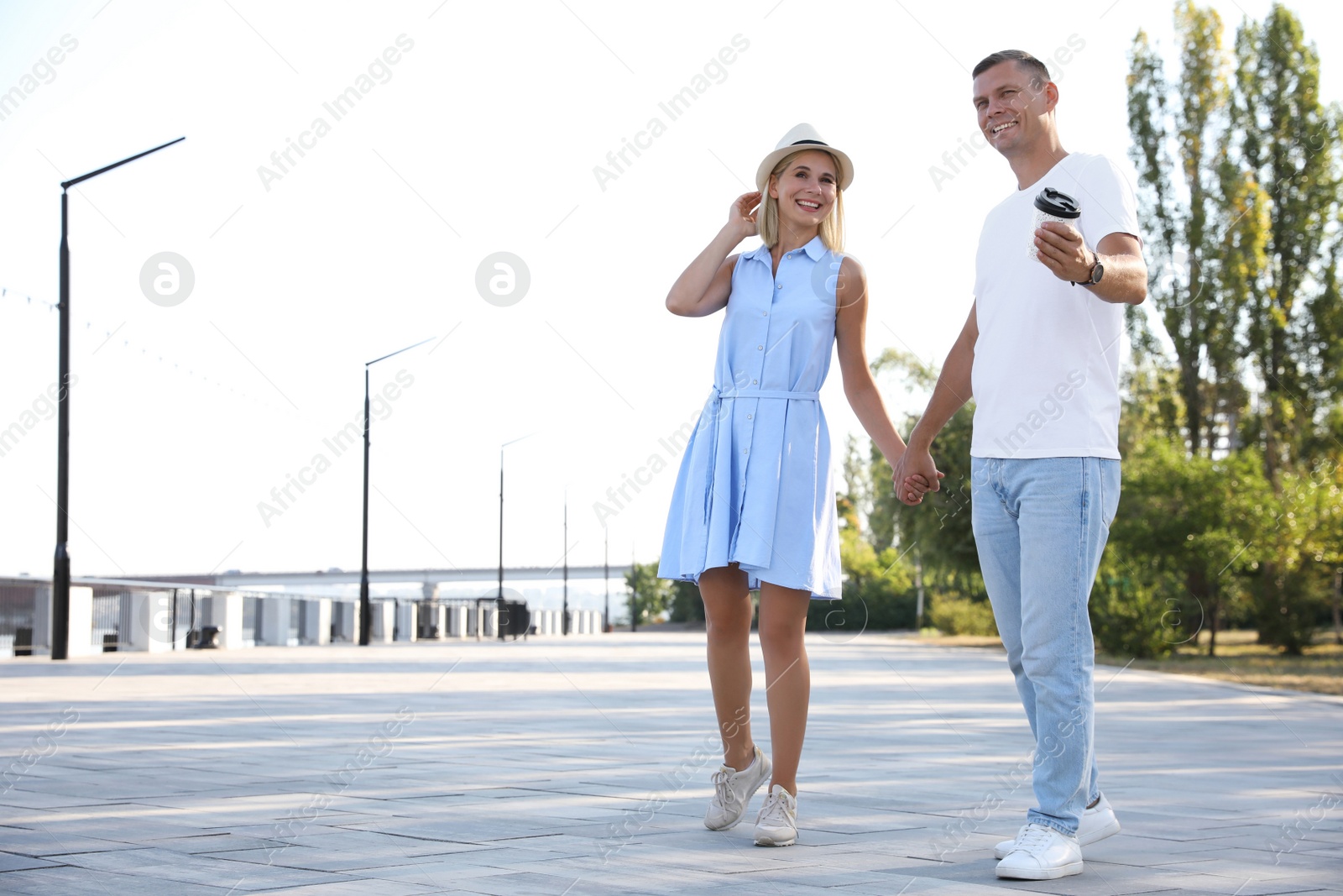 Photo of Happy couple with drink walking along city street on summer day