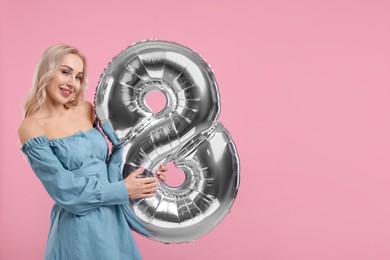 Photo of Happy Women's Day. Charming lady holding balloon in shape of number 8 on dusty pink background