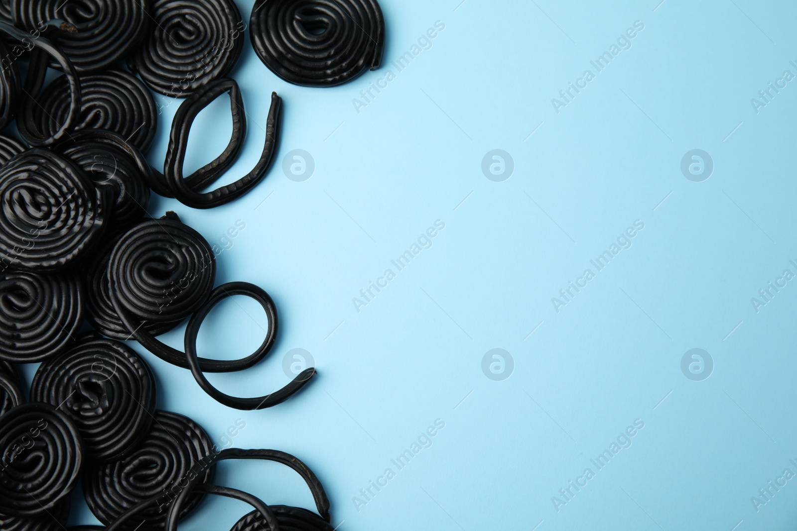 Photo of Tasty black liquorice candies on light blue background, flat lay. Space for text