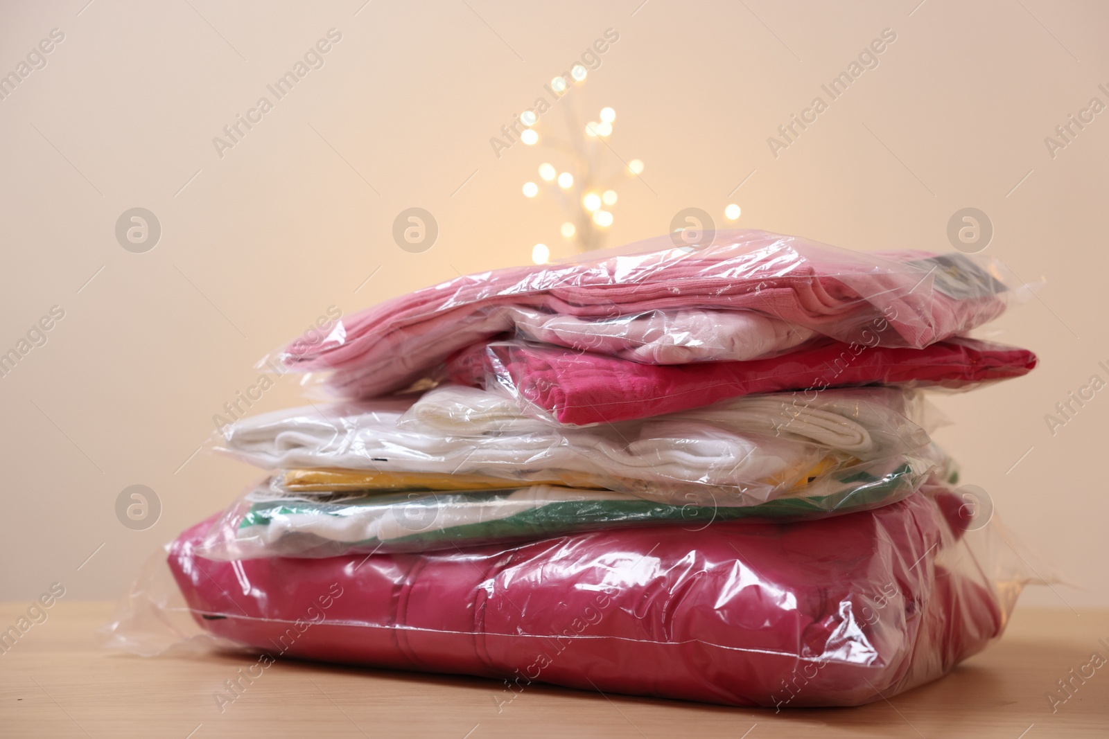Stack of folded clothes in plastic bags on wooden table against beige background, closeup Photo of Stack of folded clothes in plastic bags on wooden table against beige background, closeup