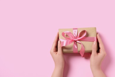 Photo of Woman holding gift box with bow on pink background, top view. Space for text