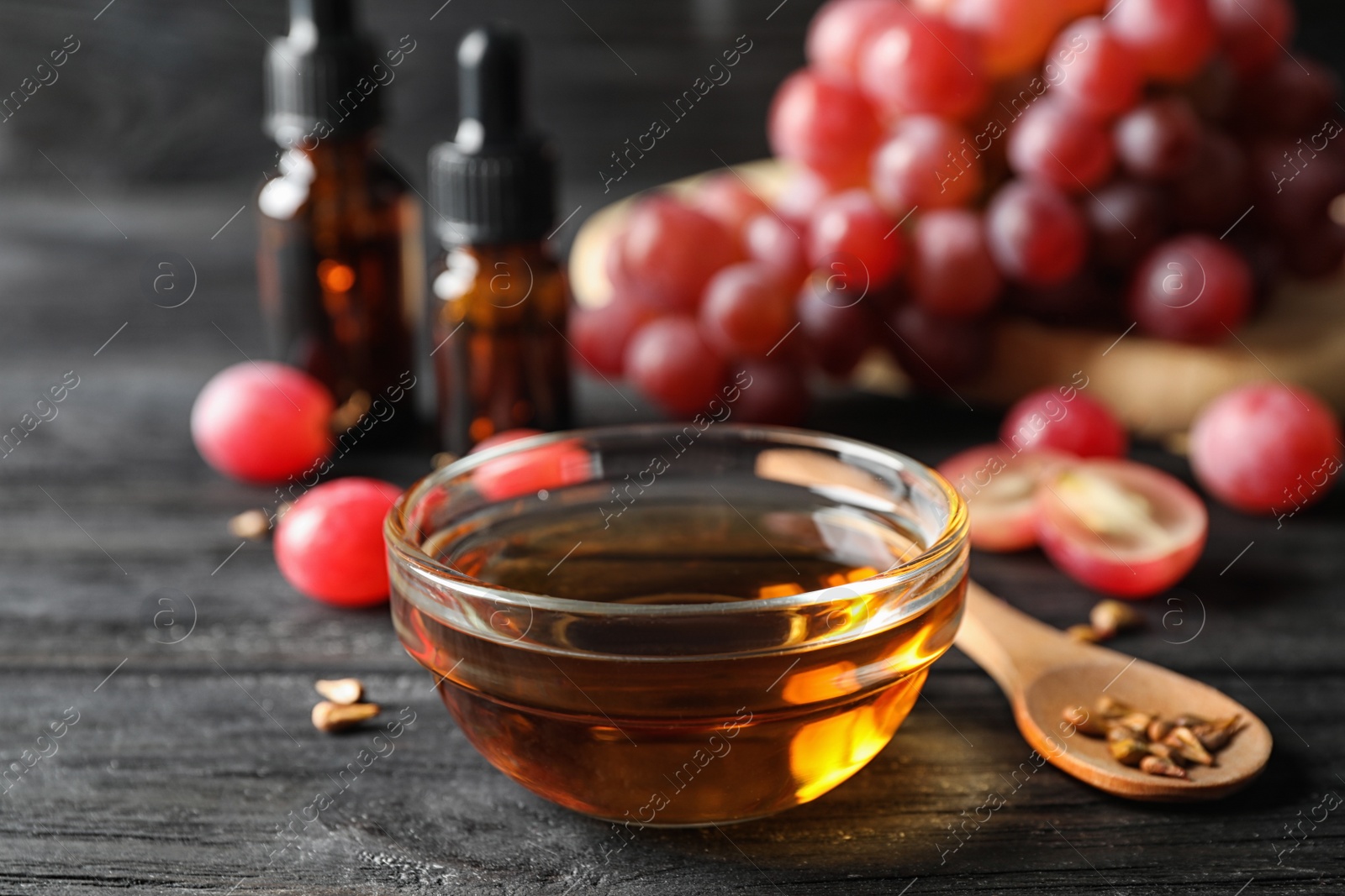 Photo of Glass bowl with natural grape seed oil on black wooden table. Organic cosmetic