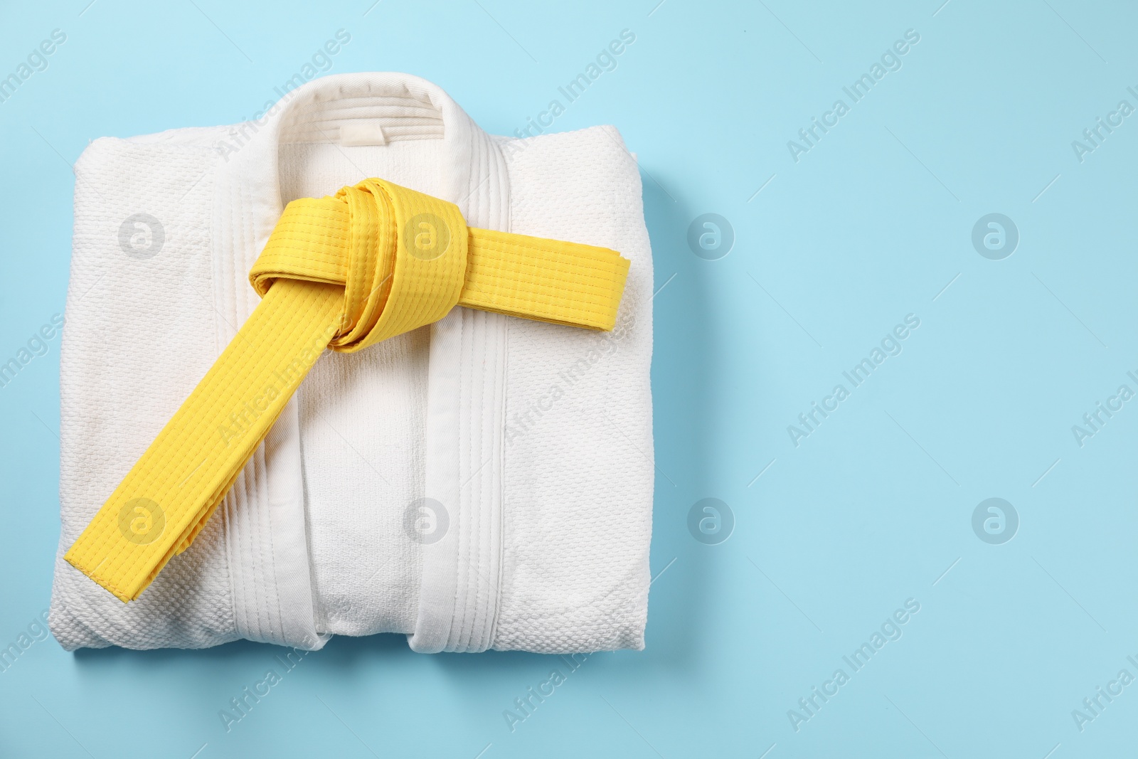 Photo of Yellow karate belt and kimono on light blue background, top view. Space for text