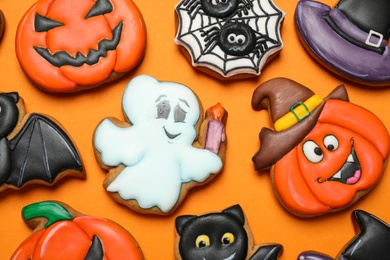 Different decorated gingerbread cookies on orange background, flat lay. Halloween celebration