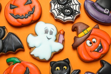 Photo of Different decorated gingerbread cookies on orange background, flat lay. Halloween celebration