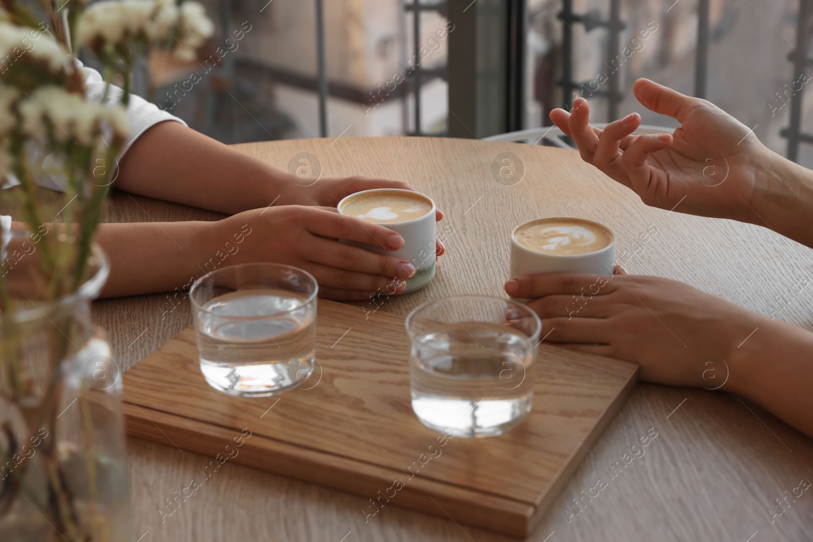 Photo of Friends drinking coffee at wooden table in cafe, closeup