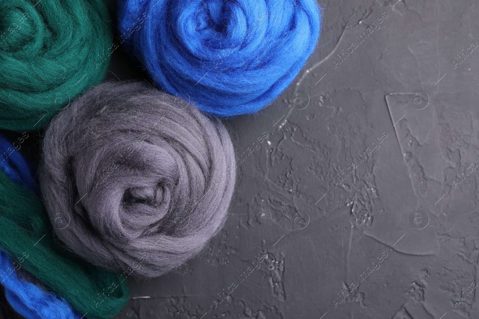 Photo of Colorful felting wool on dark textured table, flat lay. Space for text