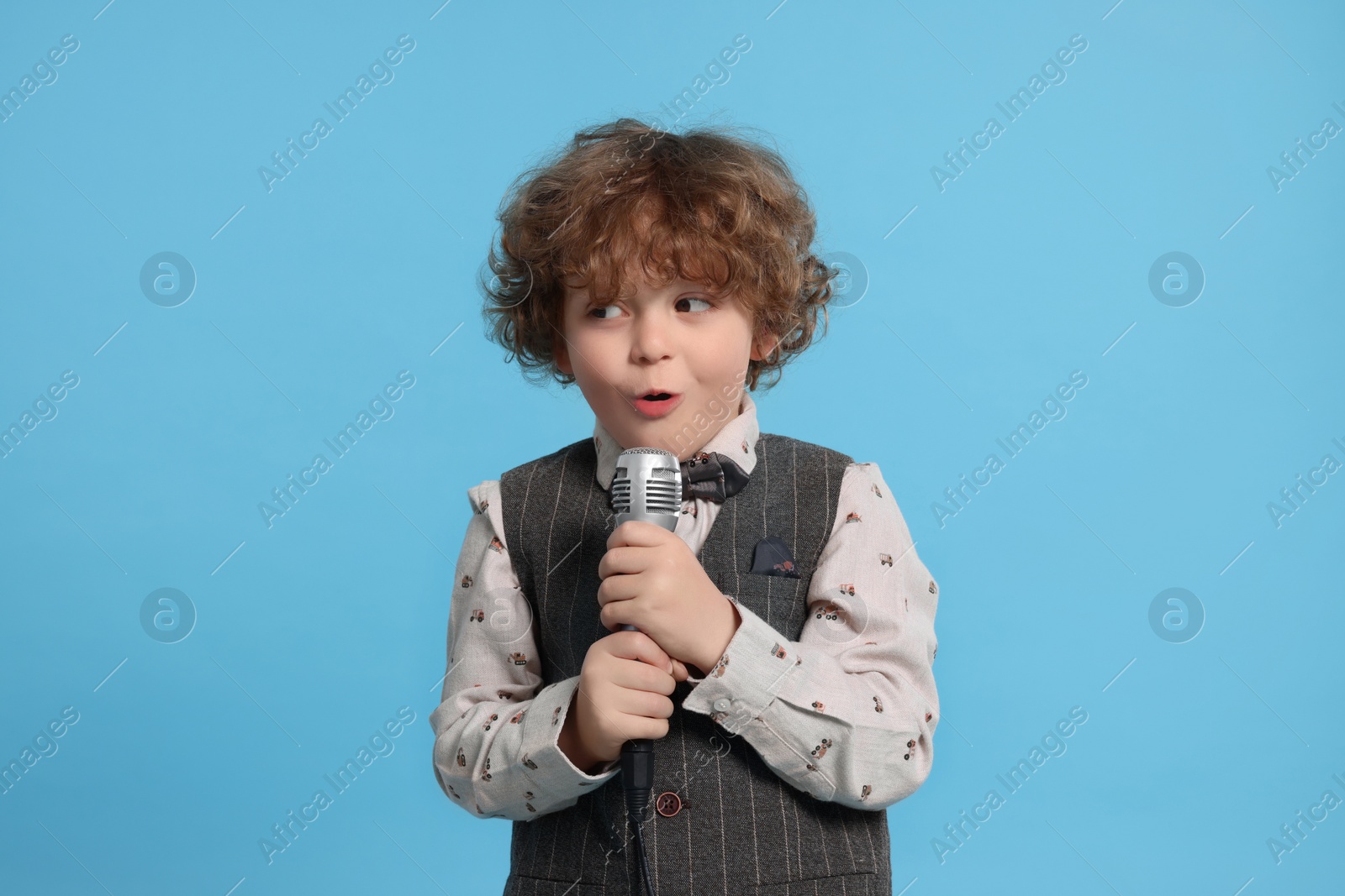 Photo of Cute little boy with microphone singing on light blue background