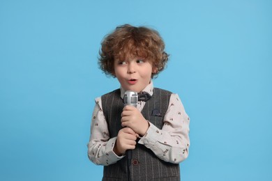 Cute little boy with microphone singing on light blue background