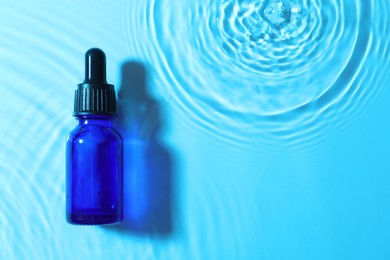 Photo of Bottle of face serum in water on light blue background, top view. Space for text