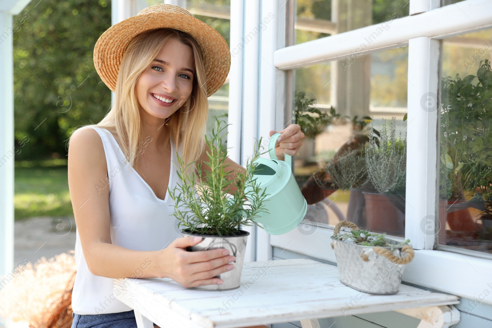 Photo of Young woman watering home plant at white wooden table outdoors