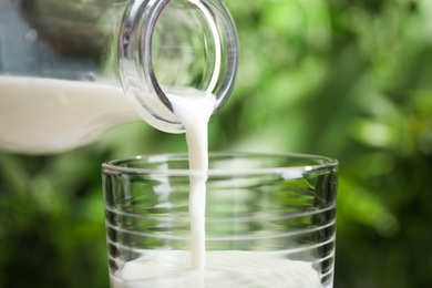 Photo of Pouring of milk from bottle into glass outdoors, closeup