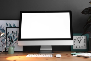 Comfortable workplace with modern computer on wooden table near black wall. Space for text