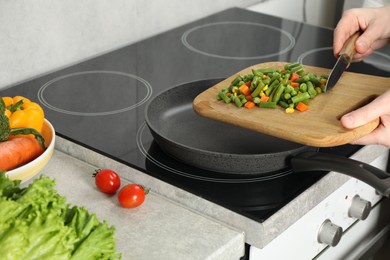 Photo of Woman putting tasty vegetable mix in frying pan at home, closeup