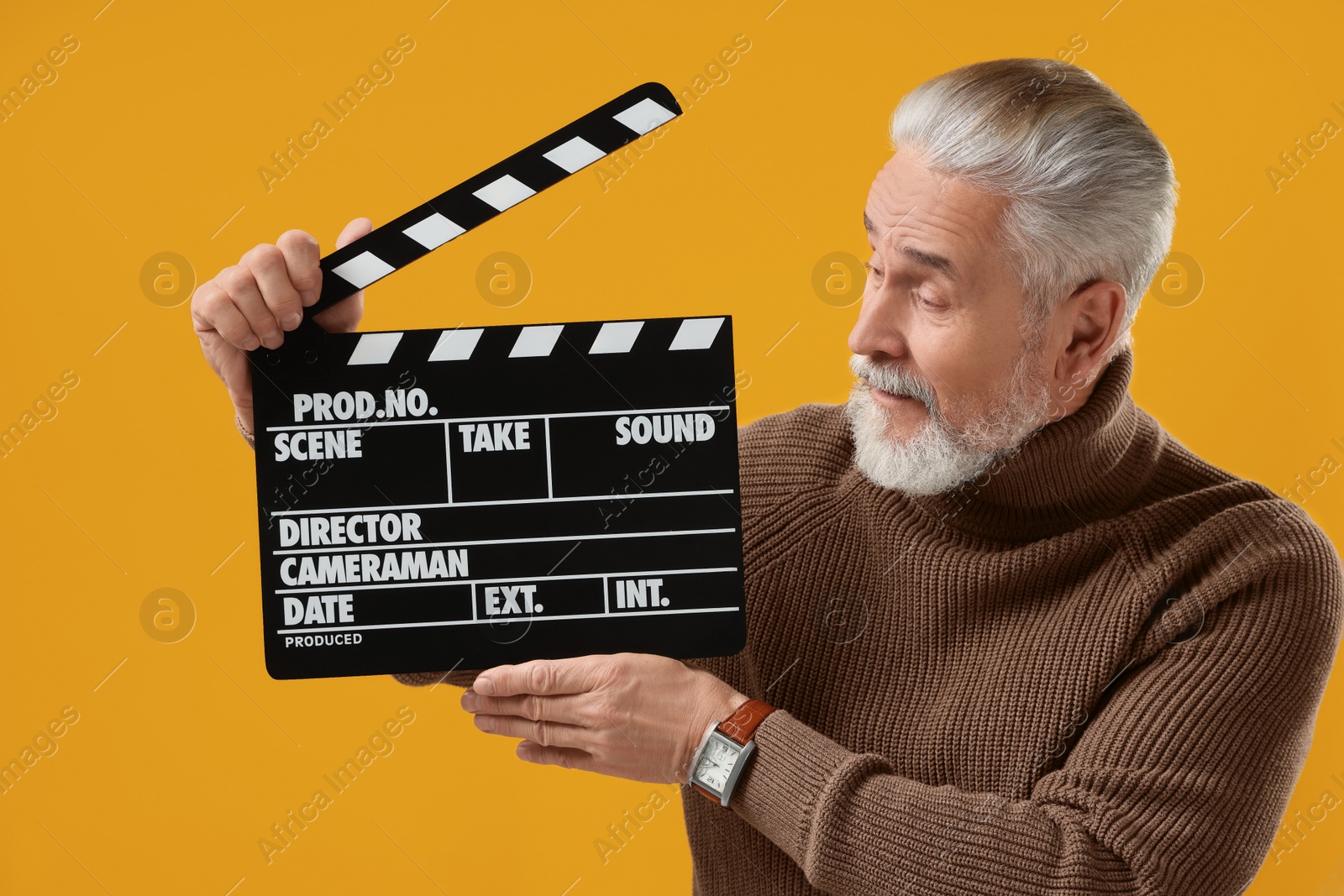 Photo of Senior actor holding clapperboard on yellow background. Film industry