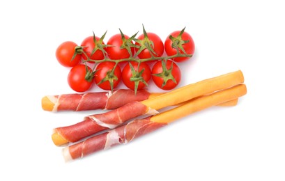 Delicious grissini sticks with prosciutto and tomatoes on white background, top view