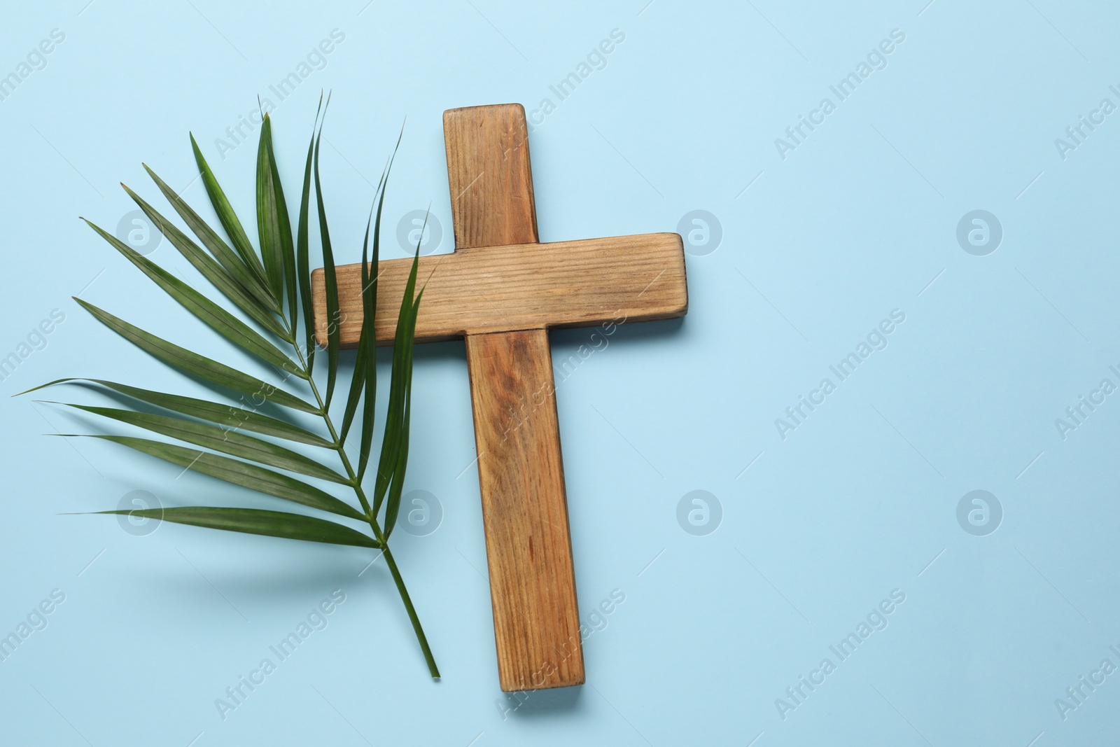 Photo of Wooden cross and palm leaf on light blue background, top view with space for text. Easter attributes